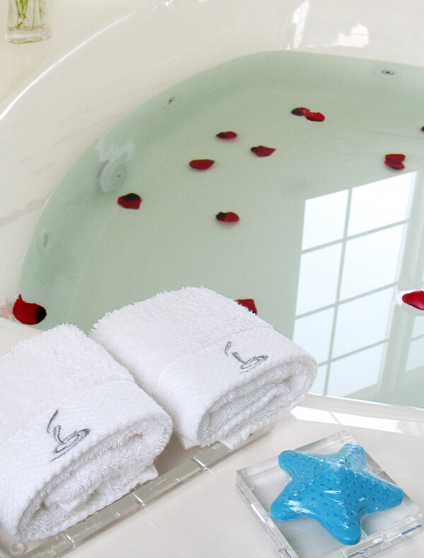 水中漂着玫瑰花瓣的浴盆旁摆放整齐的沐浴用品图片